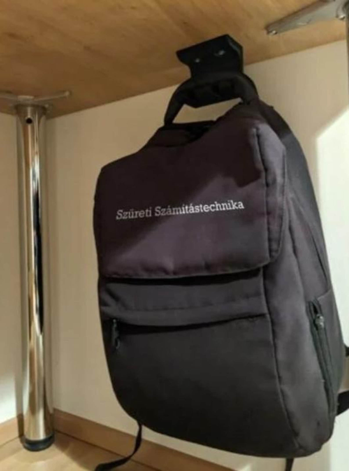 Black backpack hanging from a discreet under-desk hook