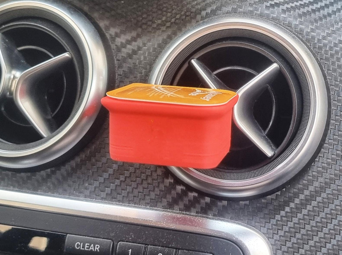 Red to-go sauce holder clipped to a car air vent
