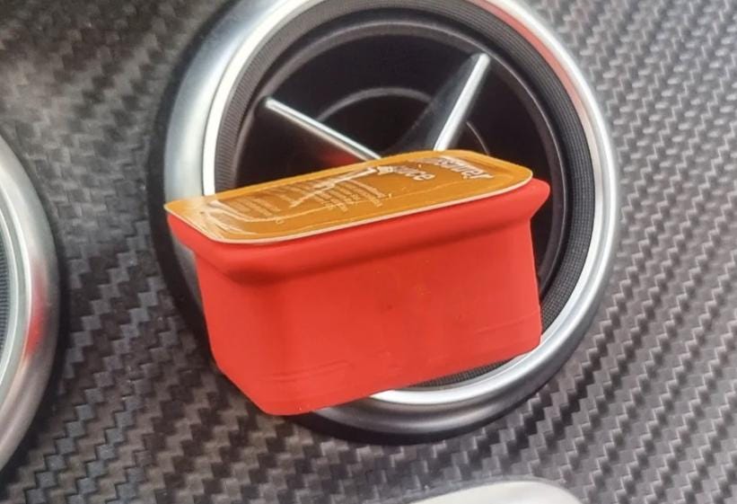 Red dipping sauce holder clipped to a round car air vent
